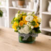 Yellow and white flower arrangement in a square glass vase with a striped ribbon
