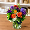 Mixed bouquet of roses, hydrangeas, and purple blooms in a glass vase