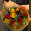 Handheld bouquet of red and yellow roses with blue thistle in brown paper