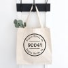 Canvas tote bag with a black printed logo hanging on a wall hook