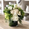 White roses and hydrangeas arranged in a dark glass vase with green succulents