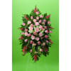 Standing floral spray of pink roses and carnations on a green backdrop