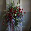 Tall floral spray with red carnations, blue flowers, and lilies on a stand