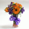 Orange and purple mixed bouquet in a clear glass vase with a purple ribbon