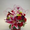 Pink lilies and red roses in a square glass vase with looping purple accents