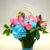 Pink roses and blue hydrangeas in a clear vase with arched handles
