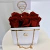 Red roses arranged in a white gift box with a gold chain handle