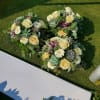 Heart-shaped floral arrangement with cream roses and white daisies on grass