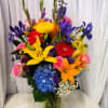 Colorful mixed bouquet in a glass vase with lilies, roses, gerberas, and hydrangea