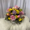 Basket arrangement of pink and lavender roses with yellow daisies and Easter eggs
