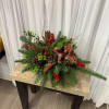 Holiday centerpiece with evergreen branches, pinecones, red berries, and a plaid bow