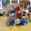 Teddy bear sitting on a toy car with red roses and pink flowers