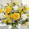Yellow roses and white flowers arranged in a clear glass vase
