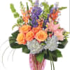 Bouquet of orange roses, pink lilies, and purple flowers in a pink vase