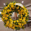 Large yellow floral wreath on a stand with a ribbon reading "From Friends"
