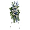 Standing floral spray with white lilies and blue flowers on a metal easel