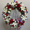 Circular wreath of red, white, and blue flowers on a stand with a ribbon bow