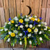 Large funeral spray with white, yellow, and blue flowers on a stand
