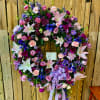 Heart-shaped floral wreath with pink, purple, and white blooms on a stand