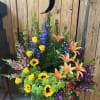Tall floral arrangement with sunflowers, roses, lilies, and blue delphinium