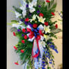 Tall standing floral spray with white lilies, red carnations, and blue ribbon