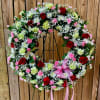 Circular floral wreath with red roses, pink carnations, and white daisies