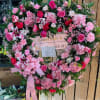 Heart-shaped floral wreath with pink roses, carnations, and lilies on an easel