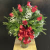 Red rose arrangement in a clear glass vase with a large red ribbon