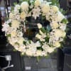 White floral wreath on a stand with roses and daisies