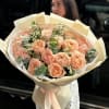 Peach rose bouquet wrapped in cream paper with a satin ribbon