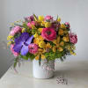 Bright mixed bouquet in a white textured vase with pink, yellow, and purple blooms