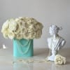 Cream rose arrangement in a turquoise box beside a white bust with pearl strands.