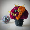 Marigold arrangement in a black vase with butterfly picks and a decorative skull beside it