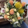 Mixed bouquet of peach roses, white orchids, and yellow pincushion blooms in a glass vase