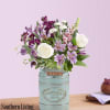 Purple and white flower arrangement in a light blue metal container.