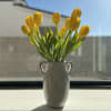 Yellow tulips in a white ceramic vase on a windowsill