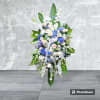 Tall standing floral spray with white and blue flowers and a white ribbon