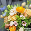 Handheld bouquet of peach roses, orange ranunculus, and pastel blooms against a dark jacket.