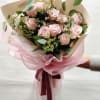 Bouquet of pale pink roses with small white filler flowers and pink wrapping