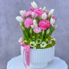 Pink and white flowers arranged in a white vase with a pink ribbon