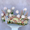 Long floral arrangement of pale roses and ranunculus in a wood container