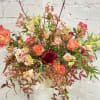 Large mixed floral arrangement in a cream vase with coral and peach blooms