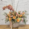 Peach and pink floral arrangement in a beige vase with tall orchid stems