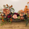 Low floral centerpiece in a woven basket with orange orchids and red roses