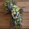 Cross-shaped floral tribute with white and blue flowers on a twig base
