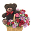 Teddy bear in a basket with mixed pink, red, and purple flowers