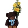 Teddy bear beside yellow roses in a glass vase