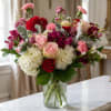 Mixed bouquet of pink, red, and white flowers in a clear glass vase
