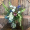 Mixed floral arrangement in a clear glass vase with white, blue, and green blooms