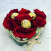 Red roses arranged with gold-wrapped chocolates in a round box